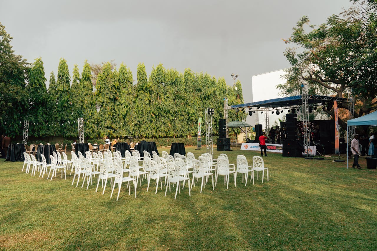 hero-contact An outdoor event venue with white chairs, stage setup, sound equipment, and greenery surrounding the space.