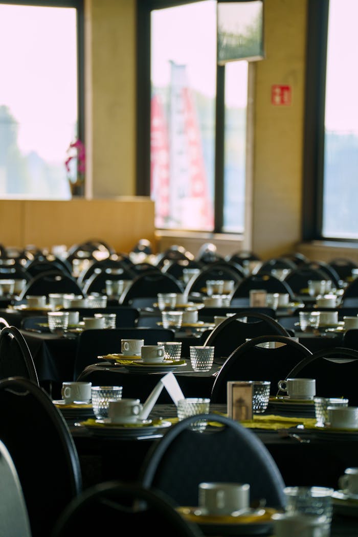 Rows of neatly arranged tables and chairs in a bright restaurant setting, with coffee cups prepared for guests.